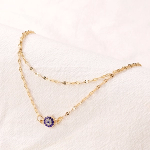 Goldene zweilagige Evil Eye Fußkette mit blauen Strasssteinen auf weißem Stoff