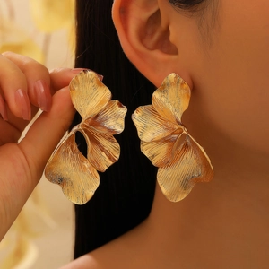Close-up of oversized golden petal earrings with textured brushed alloy finish