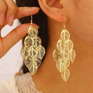 Close-up of golden leaf-shaped drop earrings with intricate hollow-out layered design