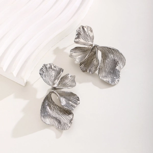 Macro detail of silver leaf earrings featuring brushed metal texture and pleated design