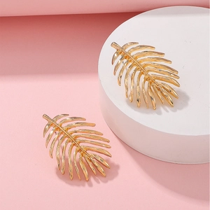 Close-up of golden hollow palm leaf earrings with detailed veins on a pink background