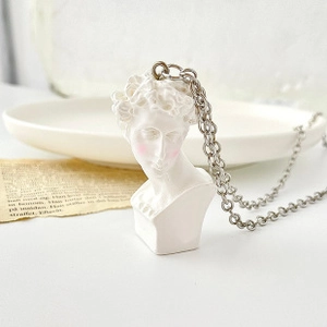 Artistic silver chain necklace featuring David bust sculpture pendant on vintage newspaper