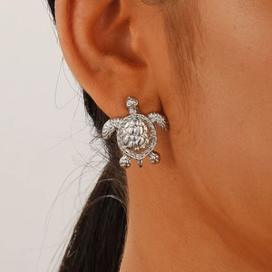 Close-up of a silver turtle stud earring with detailed shell texture on the earlobe