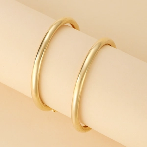Vue détaillée de deux bracelets joncs dorés polis sur un support de présentation chic