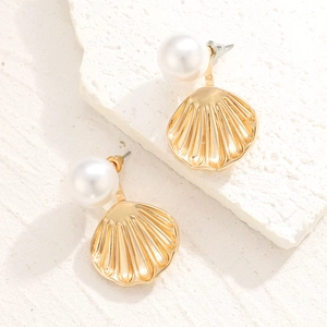Macro detail of golden spiral shell earrings with large glossy white pearls and metal texture