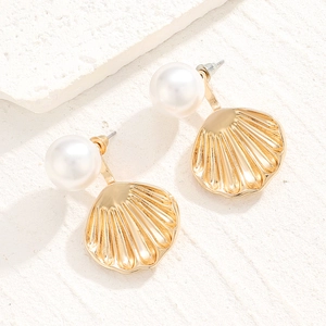 Detail of golden shell-shaped earrings with white pearls on a natural stone surface