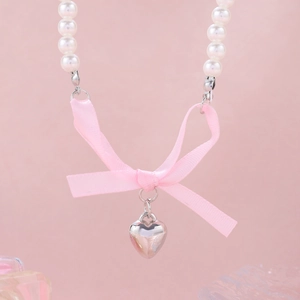 Detail of pink satin bow and silver heart pendant on a white pearl strand necklace