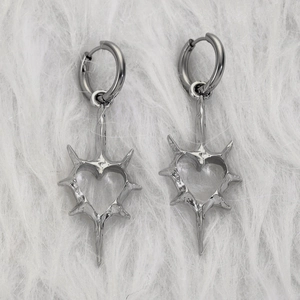 Nahaufnahme silberner Gothic-Ohrringe mit Dornenherz und Metallkreuz auf Kunstfell