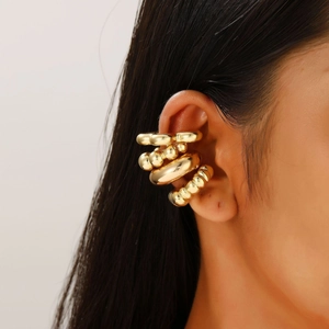 Close-up of four chunky gold-plated ear cuffs with various textures on a model's ear