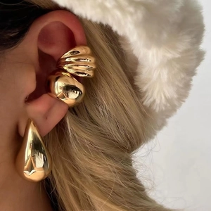 Close-up of gold drop earrings and textured ear cuffs worn with a plush white hat