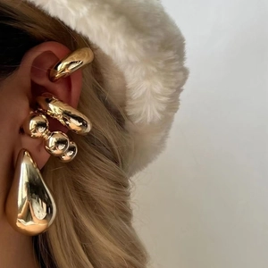 Detailed close-up of polished gold teardrop earrings and layered ear cuffs on model
