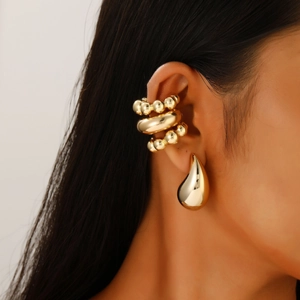 Close-up of polished gold teardrop earring and ear cuffs set on model's ear