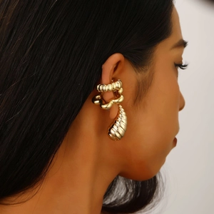 Detailed close-up of a gold ear cuff set with textured droplet earrings on a model ear