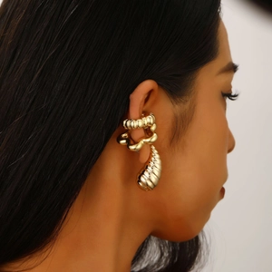 Detail of golden textured ear cuff and drop earring set on model with metallic finish