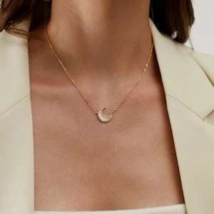 Detalle de un collar con colgante de luna con acabado blanco en cadena dorada y blazer crema