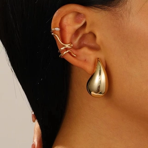 Close-up of golden teardrop earring and wavy multi-layer ear cuff with zircons