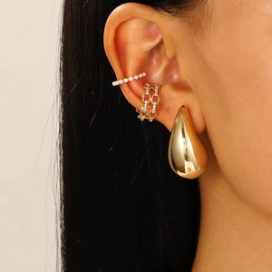 Close-up of gold teardrop earrings and layered pearl and rhinestone ear cuffs