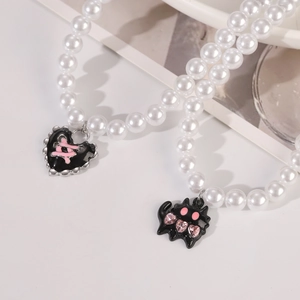 Close-up of pearl necklace featuring black gothic monster pendant and heart charms