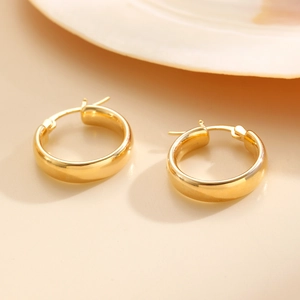 Detail of chunky gold-plated hoop earrings with polished finish and lever back closure