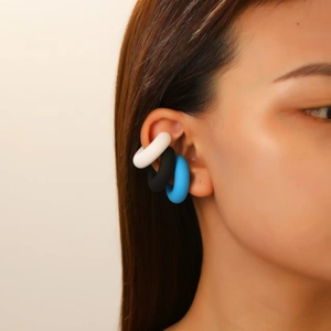 Close-up of stylish C-shaped ear cuffs set in white, black and blue on model's ear