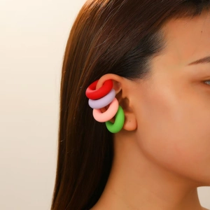 Close-up of a model wearing four colorful matte ear cuffs in red, purple, pink, and green