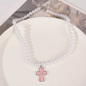 Detail shot of white faux pearl necklace with pink enamel cross pendant on a white plate