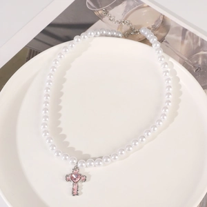 Detailed view of pearl necklace featuring a silver cross pendant and pink heart crystal