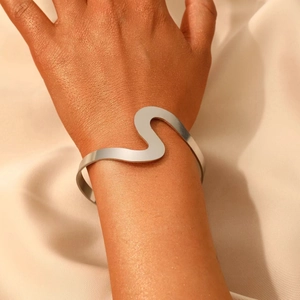 Polished silver wave cuff bracelet shown on wrist against beige silk background