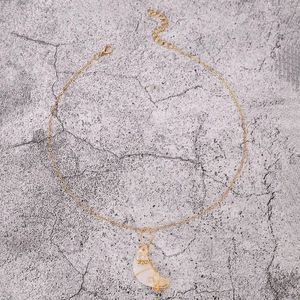 Detalle de collar con colgante de luna, hilo dorado, piedra acrílica y cierre de langosta