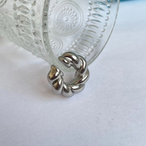 Close-up of a silver twist croissant ring with high-polish finish next to a glass