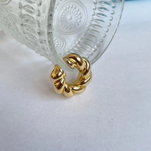 Close-up of golden hollow oval earrings with twisted texture against a glass cup
