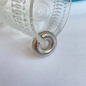 Detailed close-up of silver oval clip earrings with spiral texture on a glass rim