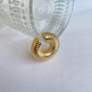 Close-up of golden ribbed ear cuff resting on clear embossed glass with sleek metal texture