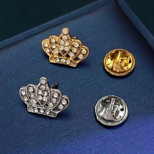 Detailed view of silver and gold crown brooches with white crystals on a blue background