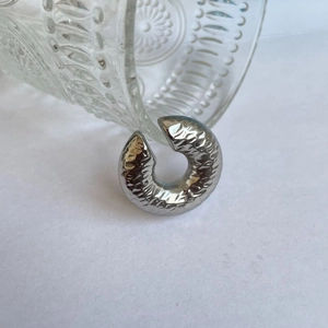 Detail of silver C-shaped ear cuff featuring a textured hammered finish and metallic luster