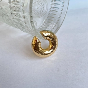 Detailed close-up of golden irregular textured ear cuff against elegant glass decor