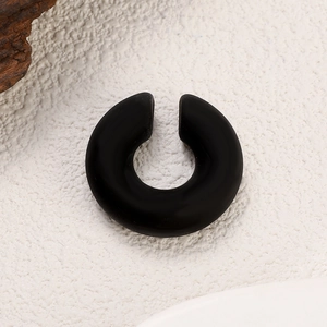 Close-up of matte black C-shaped acrylic ear cuff on a textured stone background