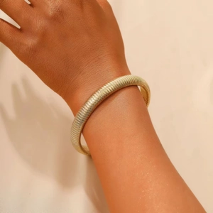 Close-up of golden multi-layer gaspipe stretch bracelet on wrist with glossy metallic texture