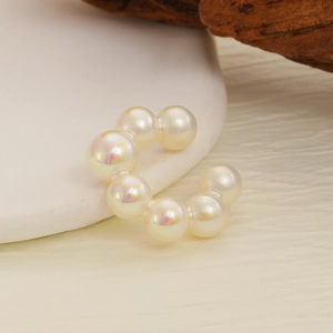 Macro detail of elegant C-shaped ear cuff with iridescent pearls on a ceramic tray