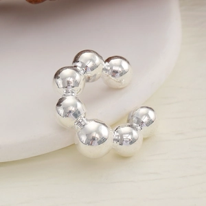 Detailed close-up of a silver polished ball ear cuff resting on a white ceramic tray