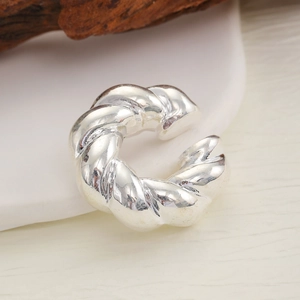 Macro detail of silver twisted rope ear cuff on a white ceramic tray with wood decor