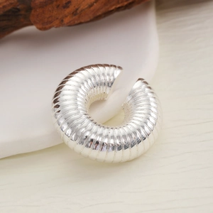 Macro shot of silver textured ear cuff with spiral pattern on wooden and ceramic base