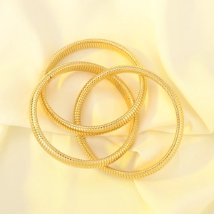 Detailed macro view of three layered gold snake-bone textured stretch bangles on silk