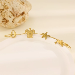 Set of 4 gold starfish turtle shell dolphin beach rings on a white ceramic display plate