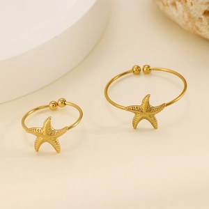 Detail of two golden starfish rings with textured marine design on a coral background