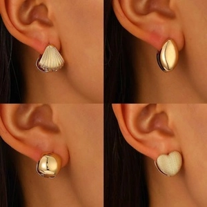 Detail shot of golden shell and heart shaped magnetic stud earrings on female model's ear