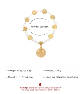 Détail des perles blanches et des médailles dorées de Saint Benoît sur le bracelet