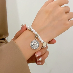 Détail du bracelet chapelet en perles blanches avec médaille de Saint-Benoît au poignet