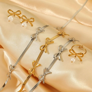 Elegantes Schmuckset aus Edelstahl mit Schleifen und Perlen auf goldenem Satinhintergrund