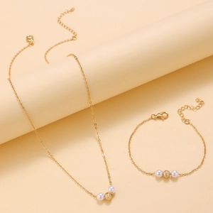 Dettaglio di un elegante set di collana e bracciale in oro con perle bianche e dorate